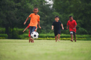 crianças jogando futebol em campo de grama
